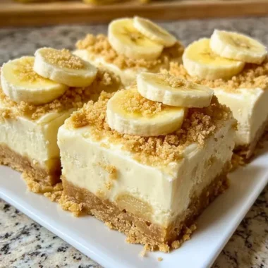 Delicious banana pudding cheesecake squares topped with whipped cream and banana slices.