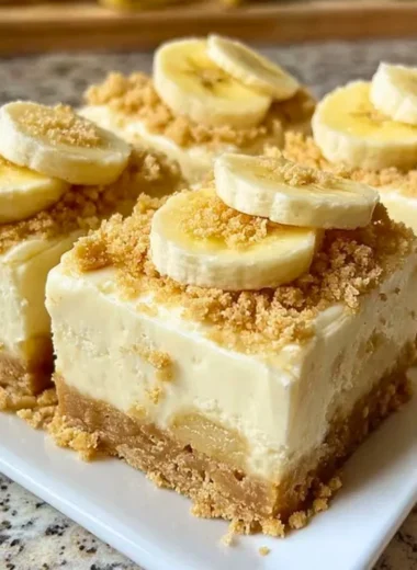 Delicious banana pudding cheesecake squares topped with whipped cream and banana slices.