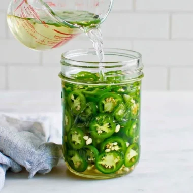Jar of homemade pickled jalapeños with spices and herbs
