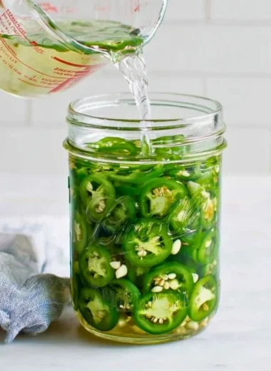 Jar of homemade pickled jalapeños with spices and herbs