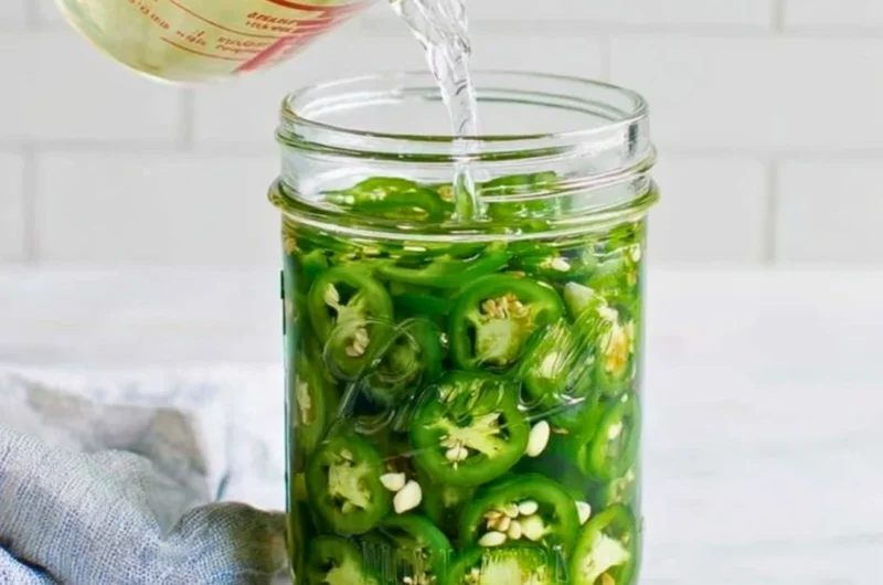 Jar of homemade pickled jalapeños with spices and herbs
