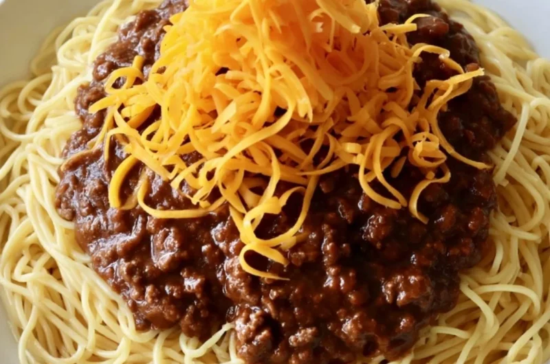 Bowl of cozy Cincinnati chili topped with cheese and onions for a comforting meal.