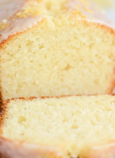 A slice of sourdough discard lemon cake on a white plate with lemon slices